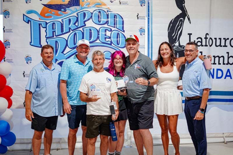 Group of people posing in front of a Tarpon Rodeo banner at an outdoor event