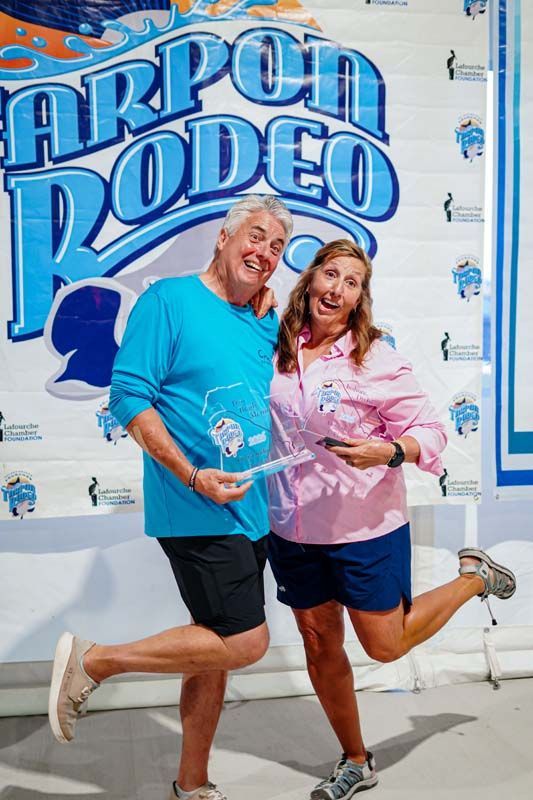 Two people posing and smiling in front of a blue “Cannon Rodeo” wall mural.