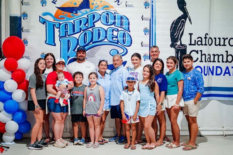 Group posing at Trop Rodeo event in front of sponsor banners and balloons