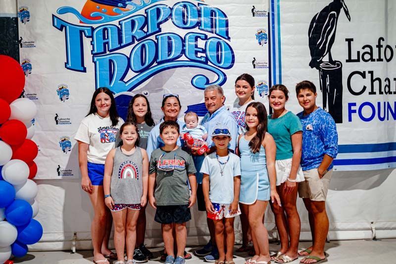 Group photo at Tarpon Rodeo booth with children and adults posing in front of sponsor banners