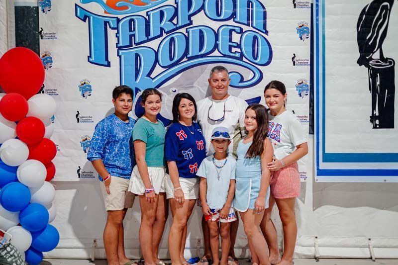 Group posing in front of a Tarpon Rodeo sign, with red, white, and blue balloon decorations.