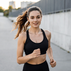 Woman jogging on a street in a black sports bra, smiling with a ponytail.