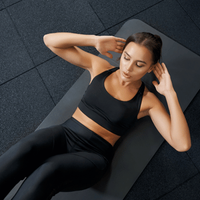 Woman doing crunches on a mat in black workout clothes on a dark gym floor
