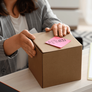 Hands placing a cardboard box with a pink “RETURN” note on a desk