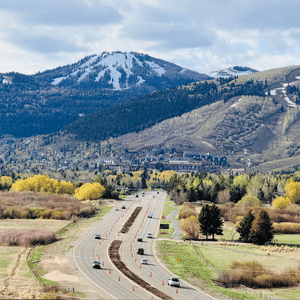 Highway through a valley with autumn trees and snowy mountains in the background