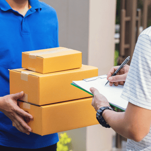 Delivery worker holding stacked cardboard boxes while another person fills out a clipboard form