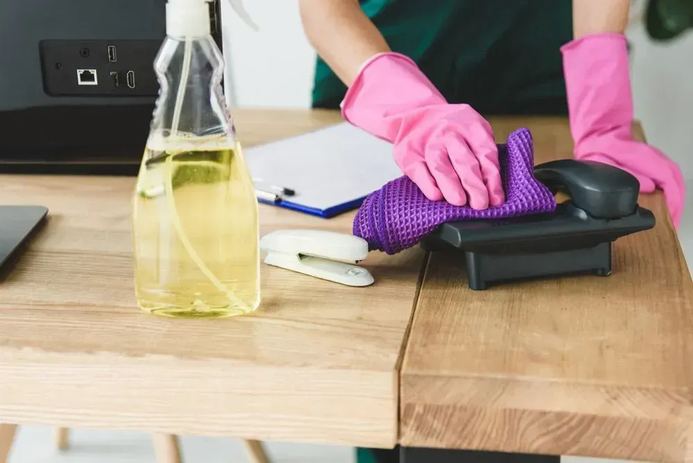 Person Wearing Pink Gloves Wiping a Desk With a Purple Cloth — Jamac Cleaning Services in Newcastle, NSW