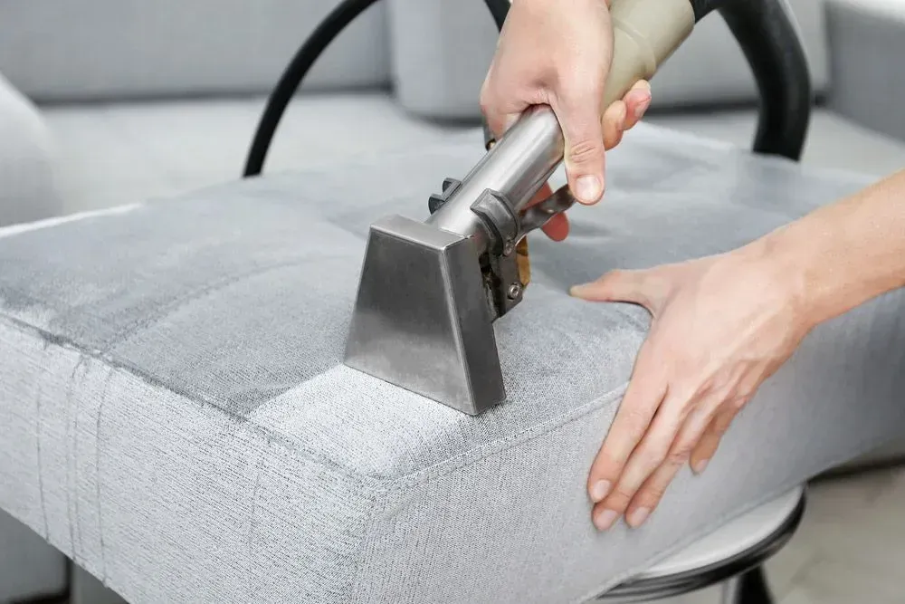 Person Using Upholstery Cleaning Tool on a Grey Couch Cushion — Jamac Cleaning Services in Swansea, NSW