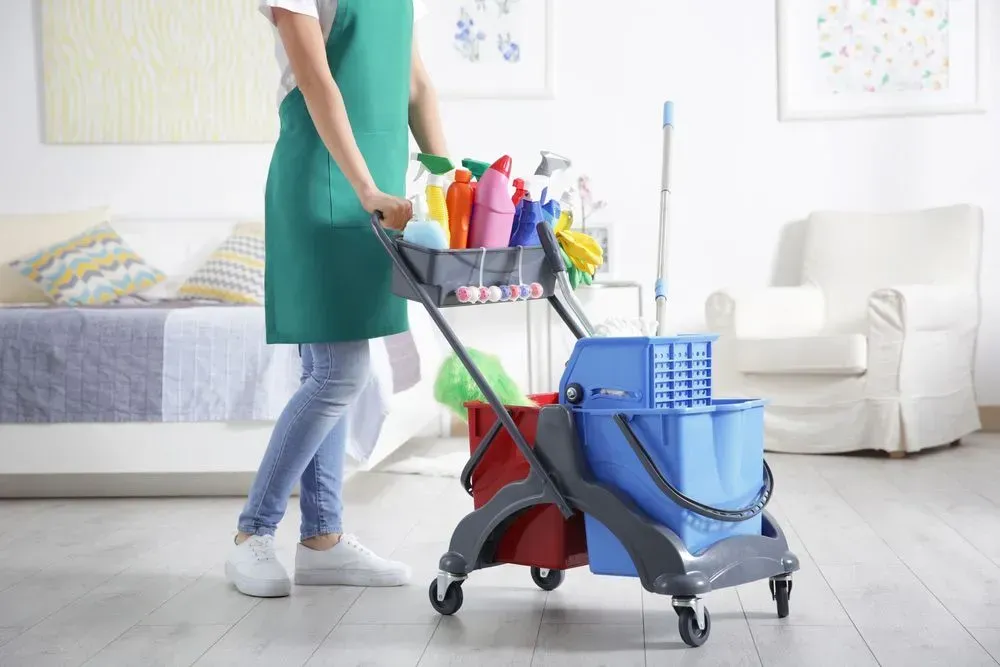 Person in Green Apron Pushing a Cleaning Cart With Supplies in a Room — Jamac Cleaning Services in East Maitland, NSW