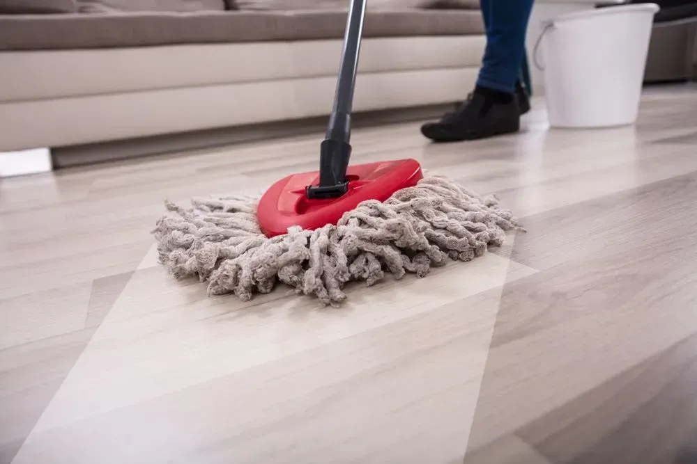 A Person Mopping a Light-colored Floor With a Red Mop — Jamac Cleaning Services in East Maitland, NSW