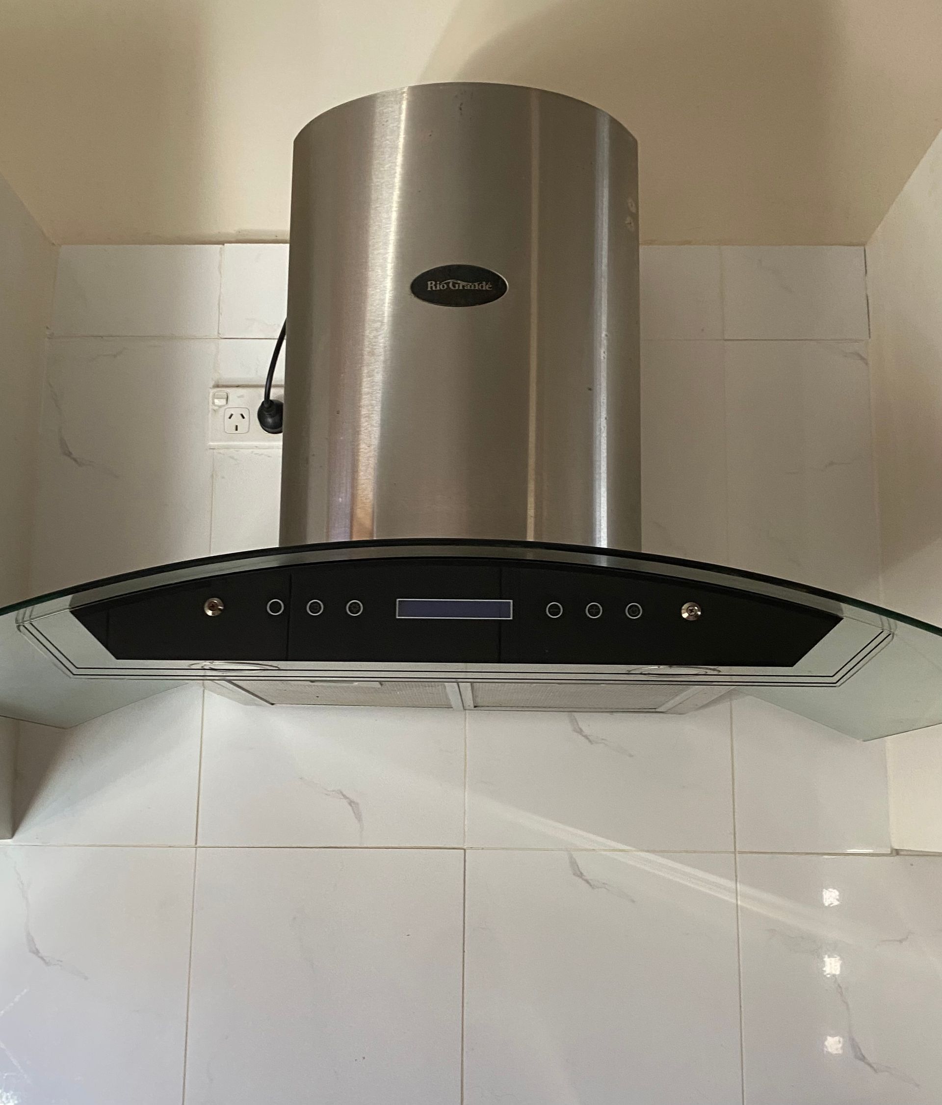 Stainless steel kitchen range hood mounted above a black glass control panel