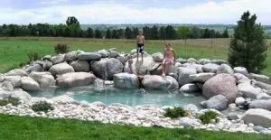 A couple of people standing on top of a rocky pond.