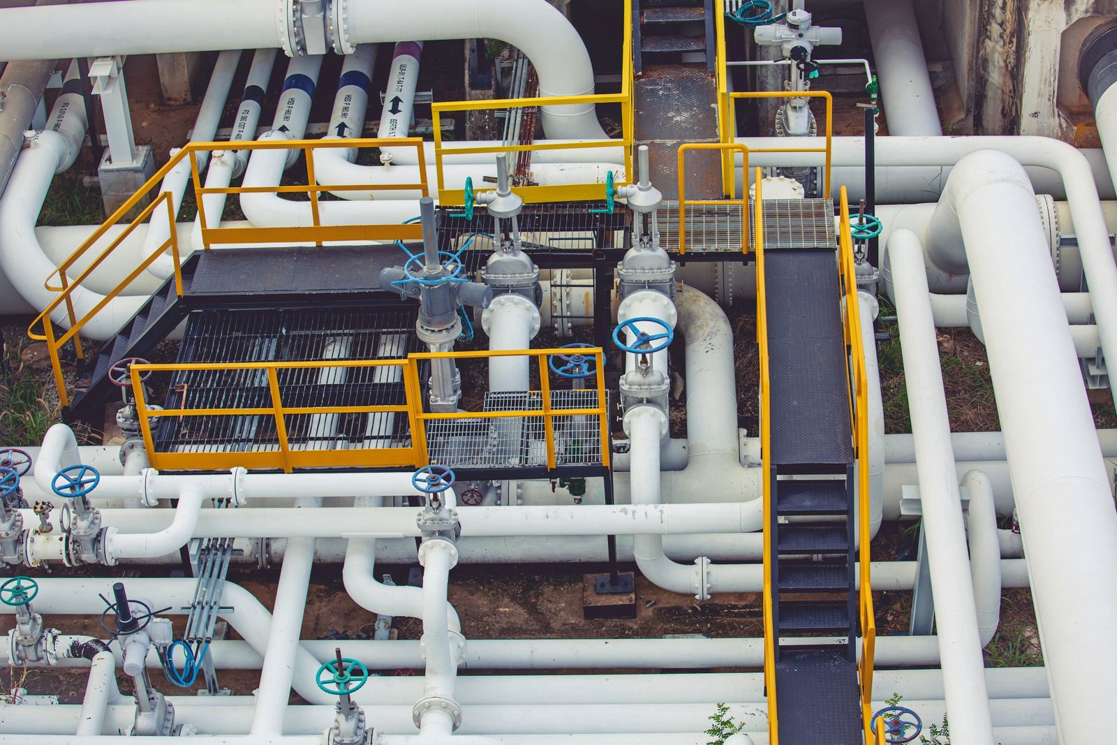 Overhead view of a network of white pipes with valves and a yellow metal platform.