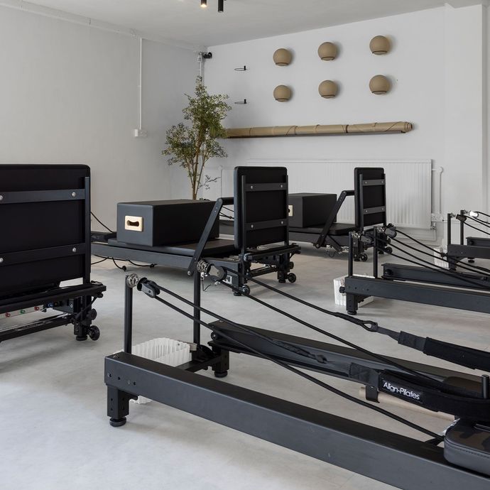 Person using a pilates reformer machine, leg extended with foot in a strap.