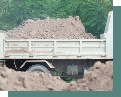 A dump truck filled with dirt is driving down a dirt road.