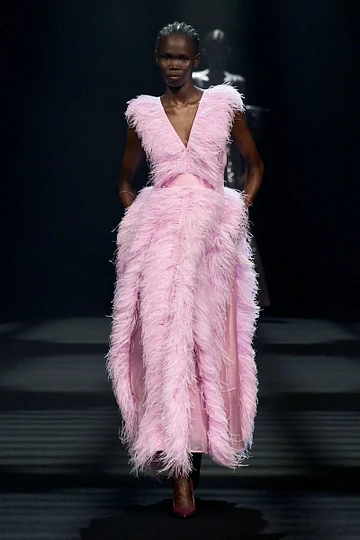 A model is walking down the runway wearing a pink feathered dress.