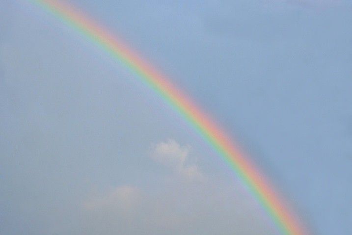 A vibrant rainbow curves across a light blue sky with a few wispy clouds.