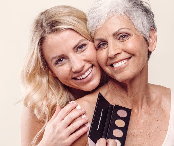 Two people embracing and smiling while holding a small rectangular makeup palette with four circular eyeshadow pans.