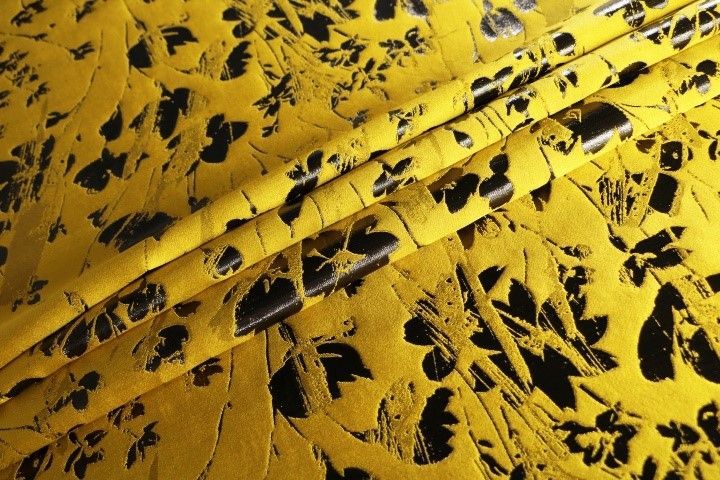 A close up of a yellow fabric with black leaves on it