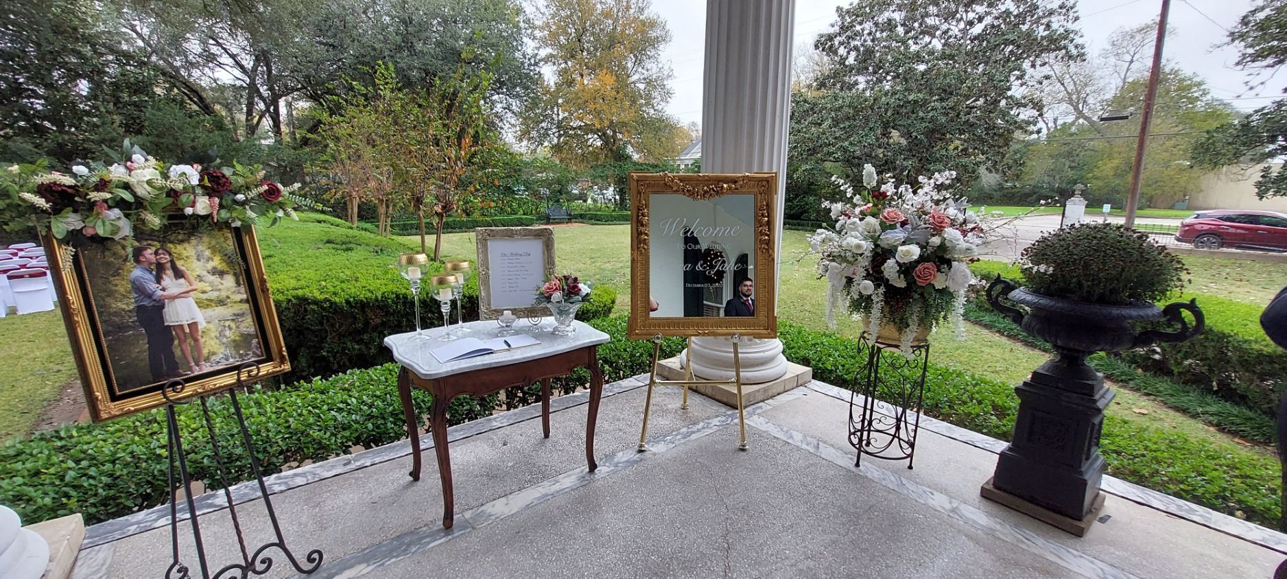 a porch with white pillars, mirror and large plants decorated for wedding.