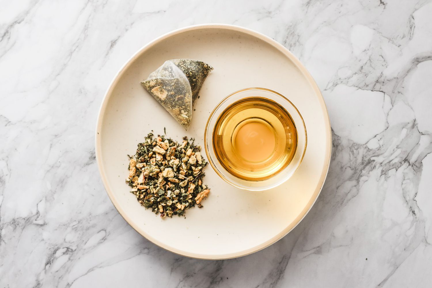 淺色大理石桌面上放著一個茶包、一小碗散裝茶葉和一杯泡好的茶。