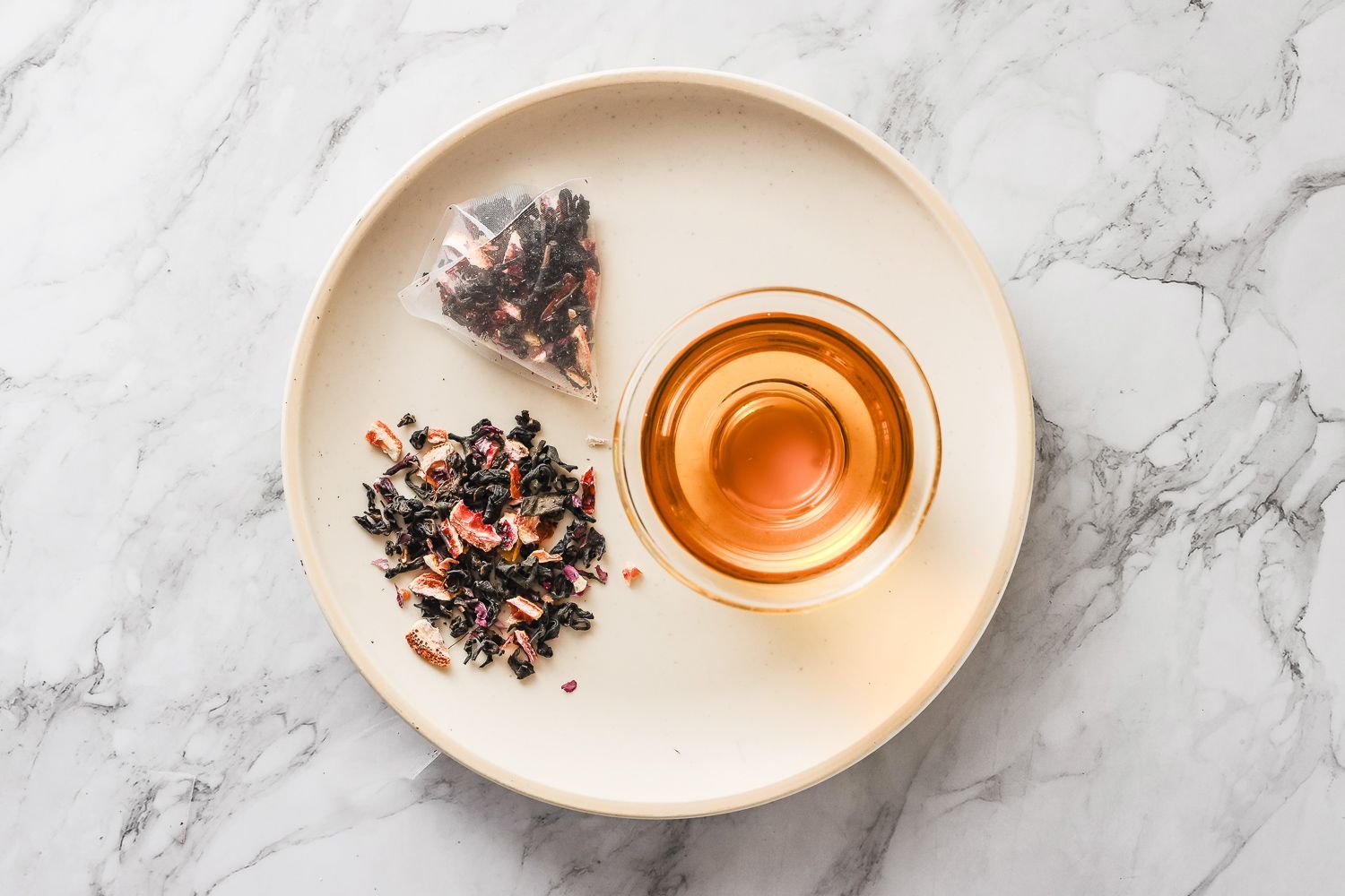 大理石檯面上放著一個茶包、一小碗乾散茶和一杯泡好的茶。