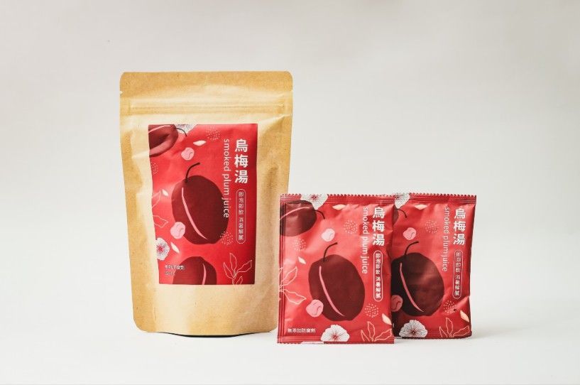 一個大的棕色紙袋和兩個較小的紅色紙袋，裡面裝著乾梅子，紙袋上印有紅色和白色的植物圖案。