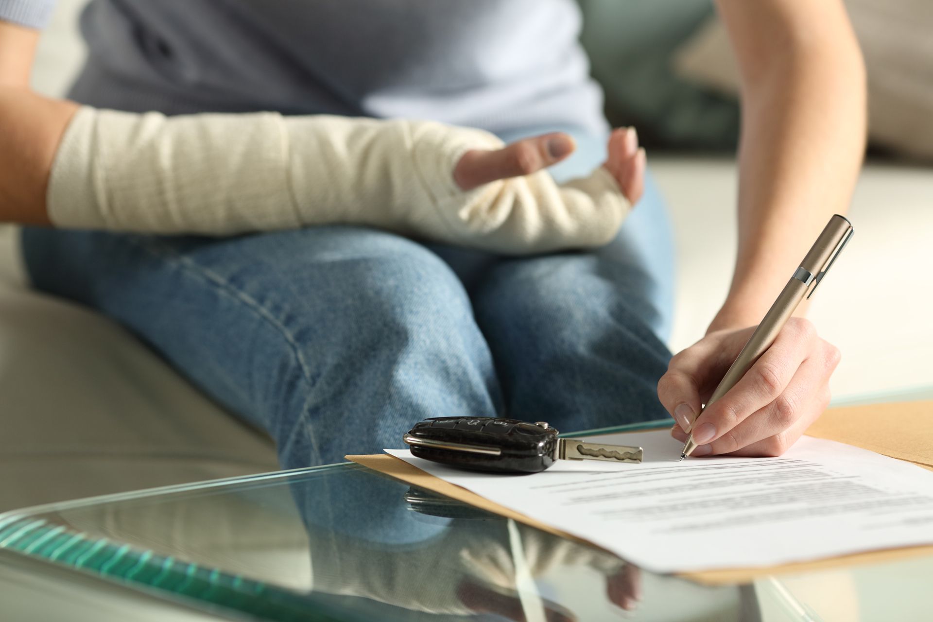 Person with arm in cast signing paperwork, car keys on table.