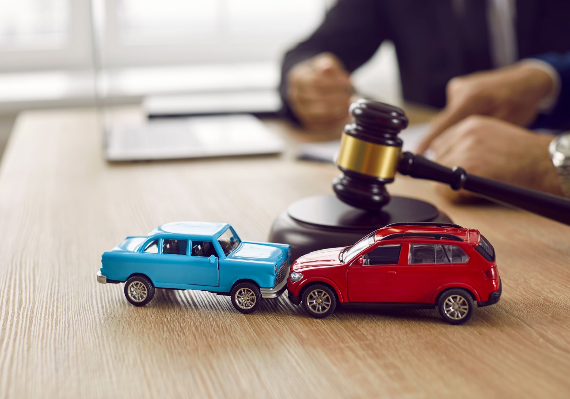 Toy cars in a collision with a gavel on a desk, a person in a suit in the background.
