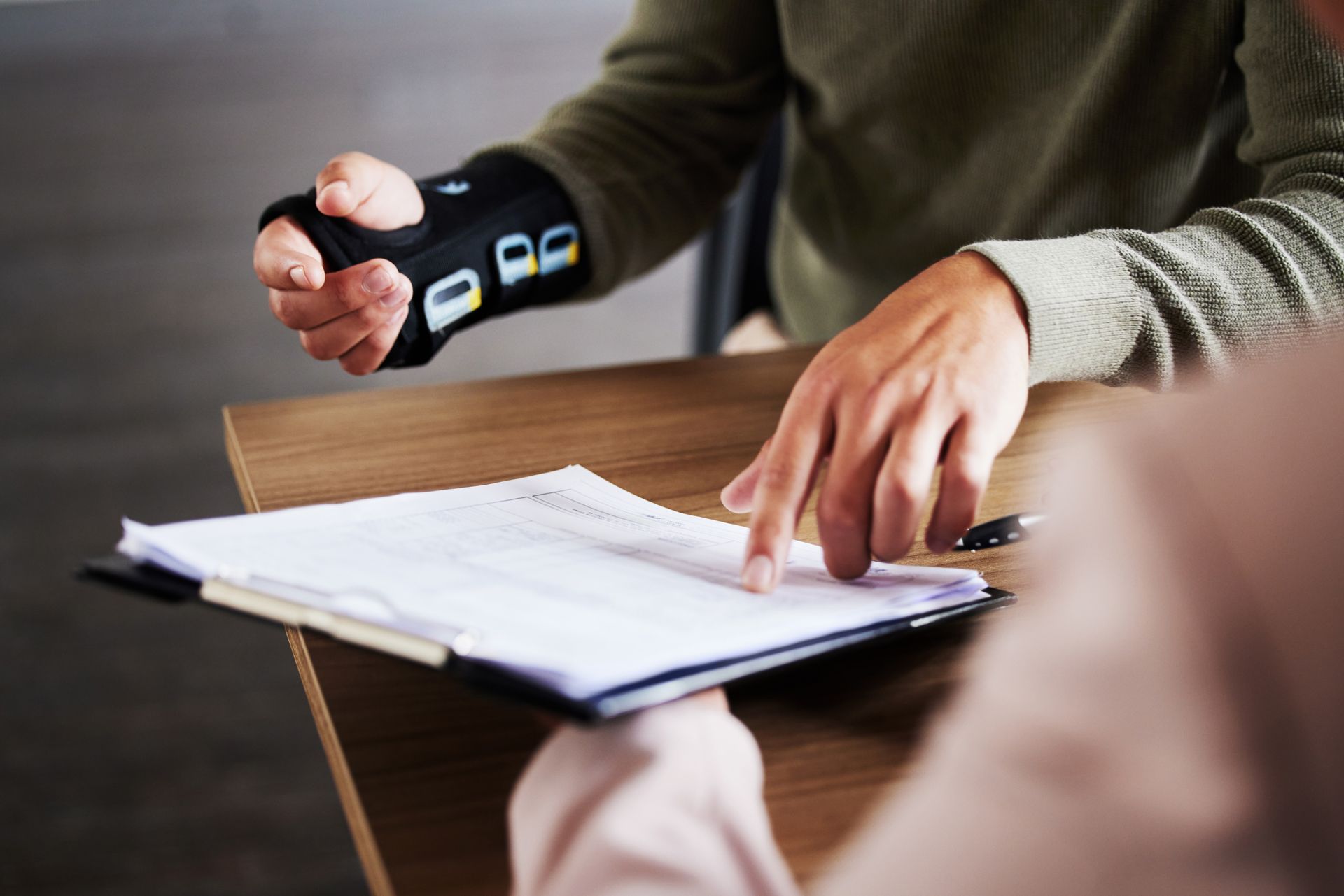 Person wearing a wrist device, pointing at document on a wooden table.