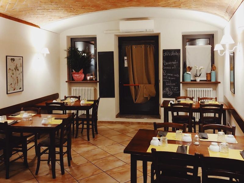 Terrazza esterna del ristorante con tavoli bianchi e sedie rosa accanto a muri in pietra e vegetazione.