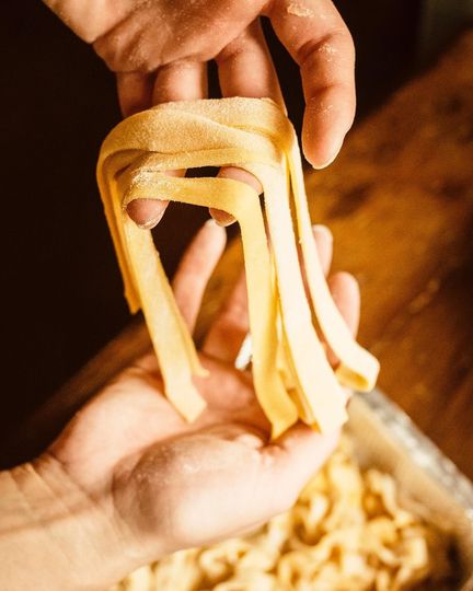 Pasta con gamberi rossi e basilico su un piatto bianco, con un bicchiere di vino bianco sullo sfondo.