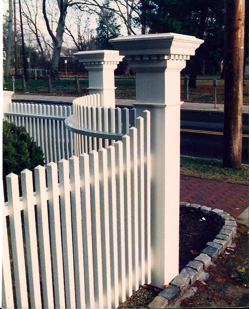 A white picket fence surrounds a brick walkway