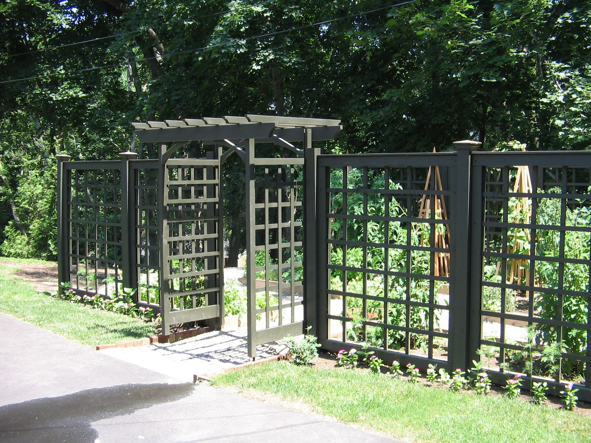 A black fence surrounds a garden with trees in the background