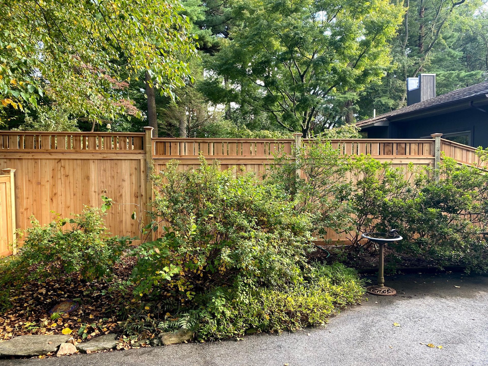A wooden fence is surrounded by trees and bushes in front of a house.
