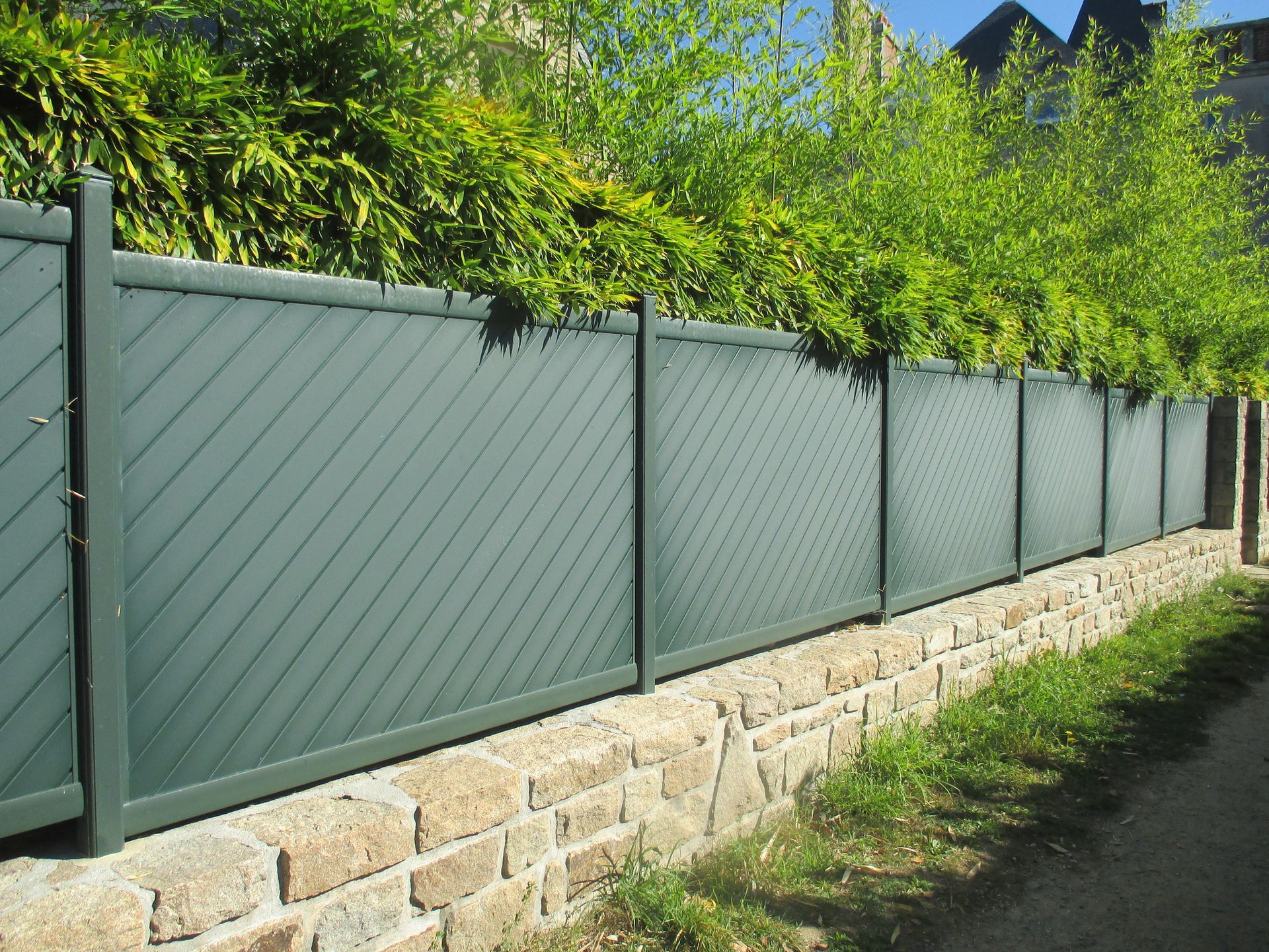 Green PVC fence propped on top of a stone wall as it encloses a garden.