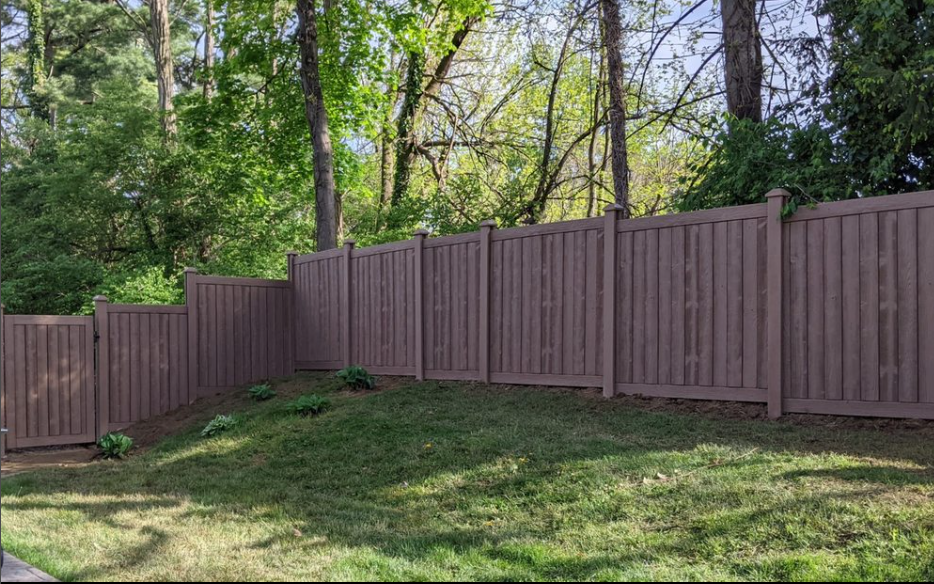 A wooden fence surrounds a lush green yard with trees in the background.