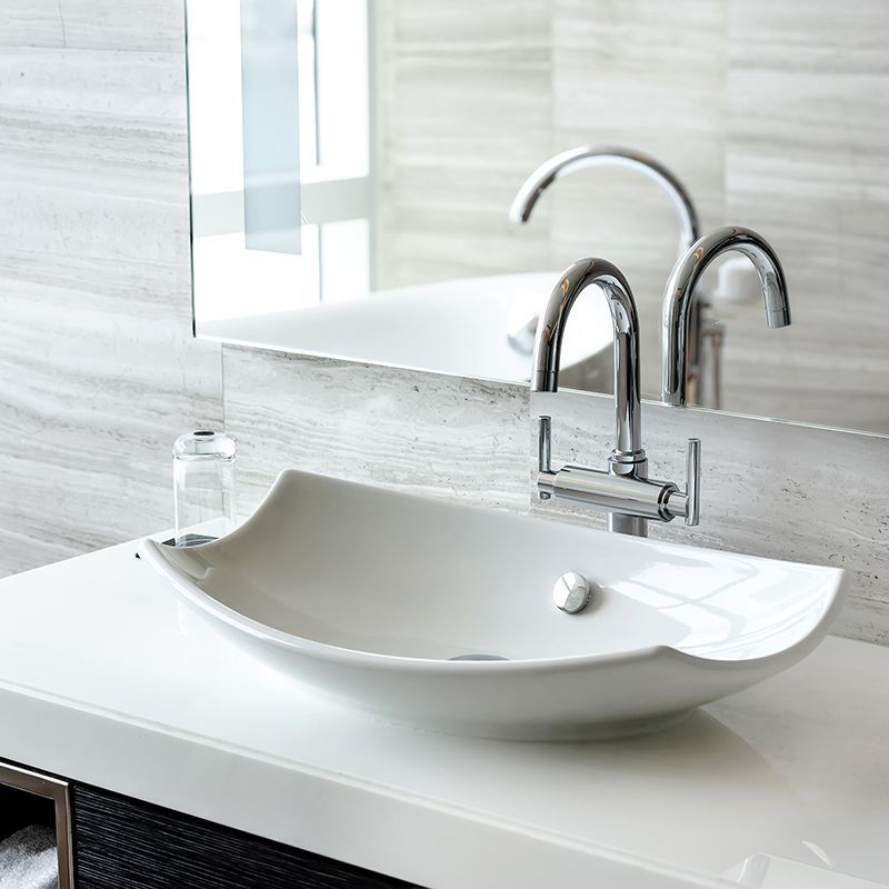 White oval vessel sink with chrome faucet, on a white countertop, reflecting in a mirror.