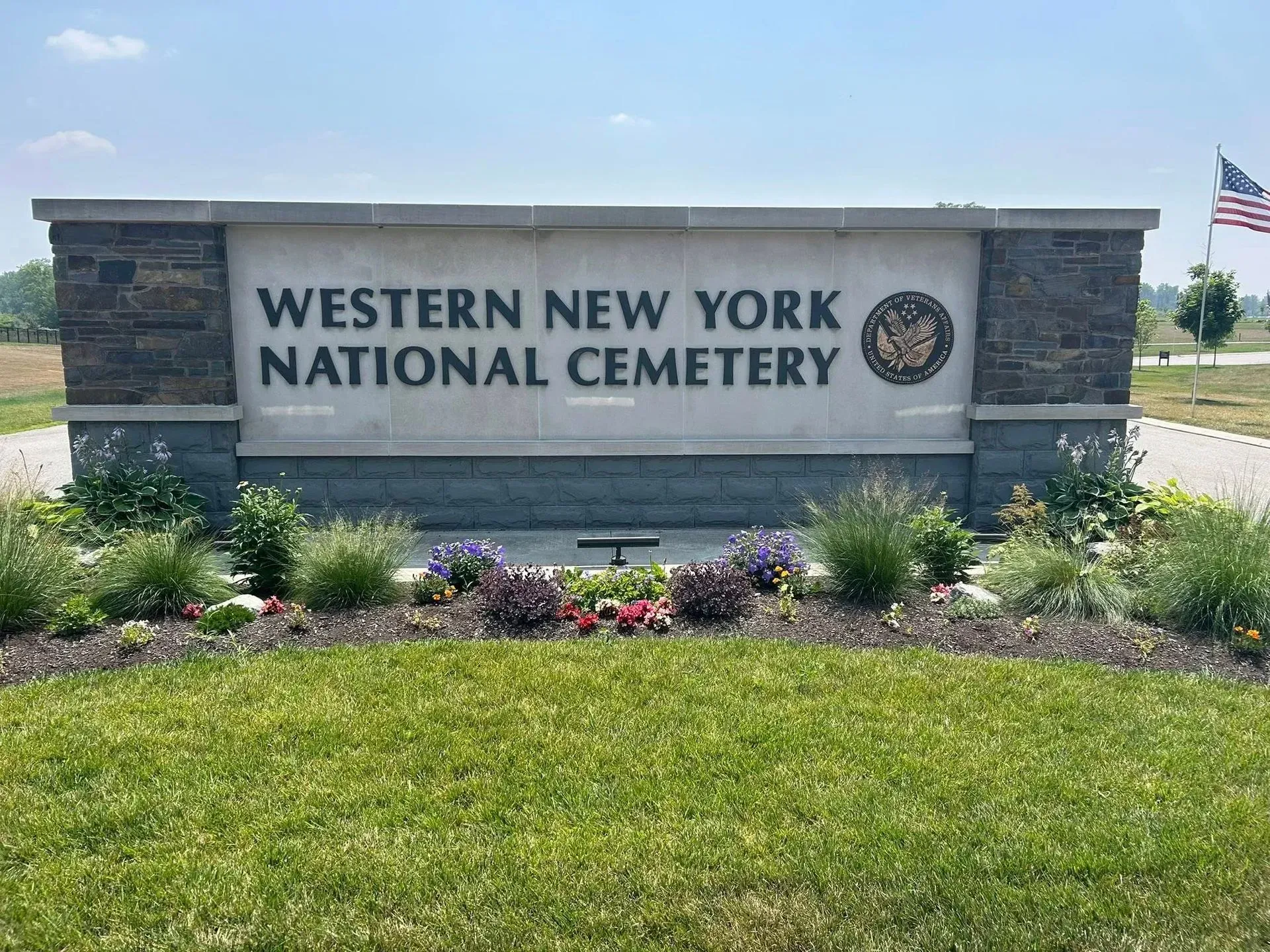 Western New York National Cemetery sign beside flowers and green lawn under a bright sky
