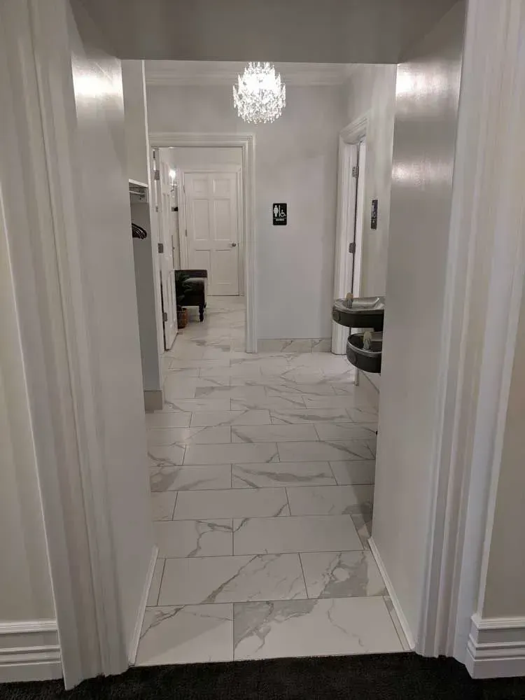 Hallway with white walls, marble-pattern tile floor, and a chandelier hanging overhead.