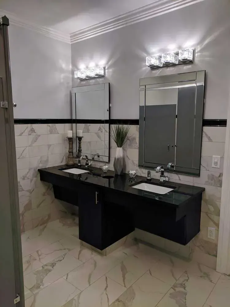 Modern bathroom vanity with double sinks, large mirrors, marble-patterned walls, and a tiled floor