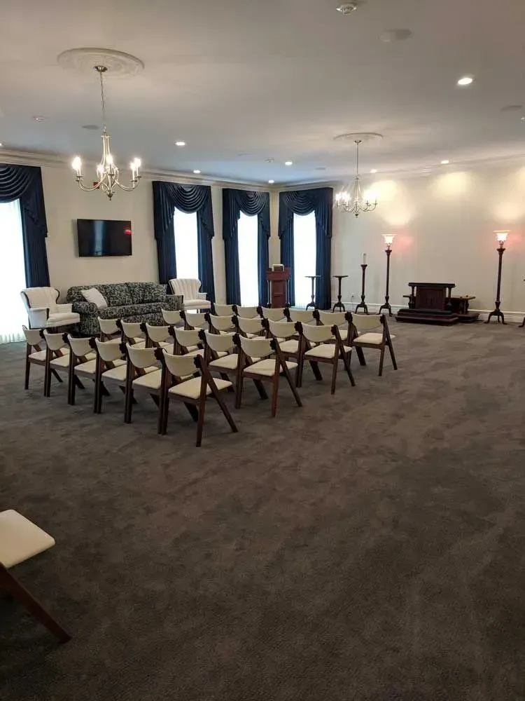 Empty chapel with rows of wooden chairs facing a small altar in a carpeted room.