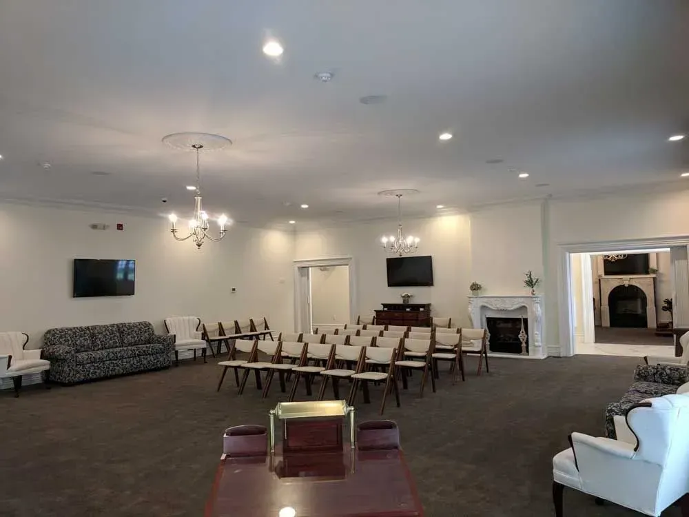 Spacious white banquet hall with rows of chairs, sofas, chandeliers, and a fireplace.