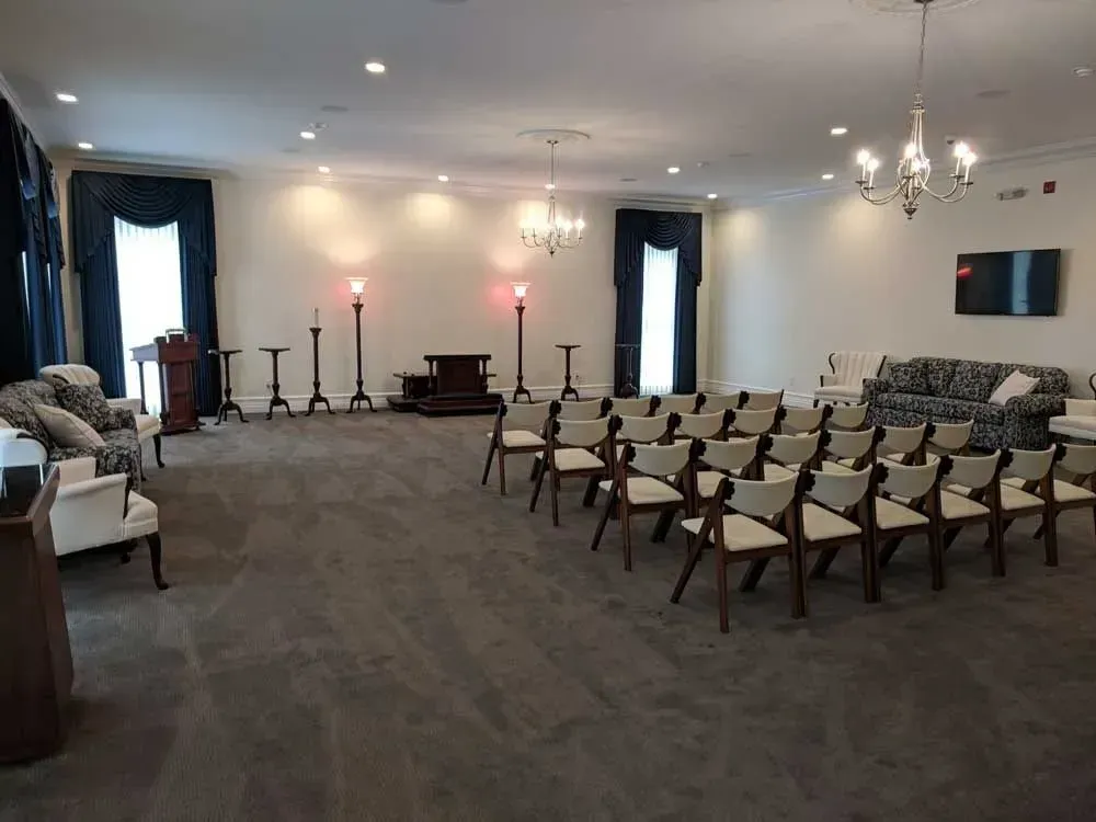 Empty banquet hall with rows of chairs facing a front wall and soft chandelier lighting