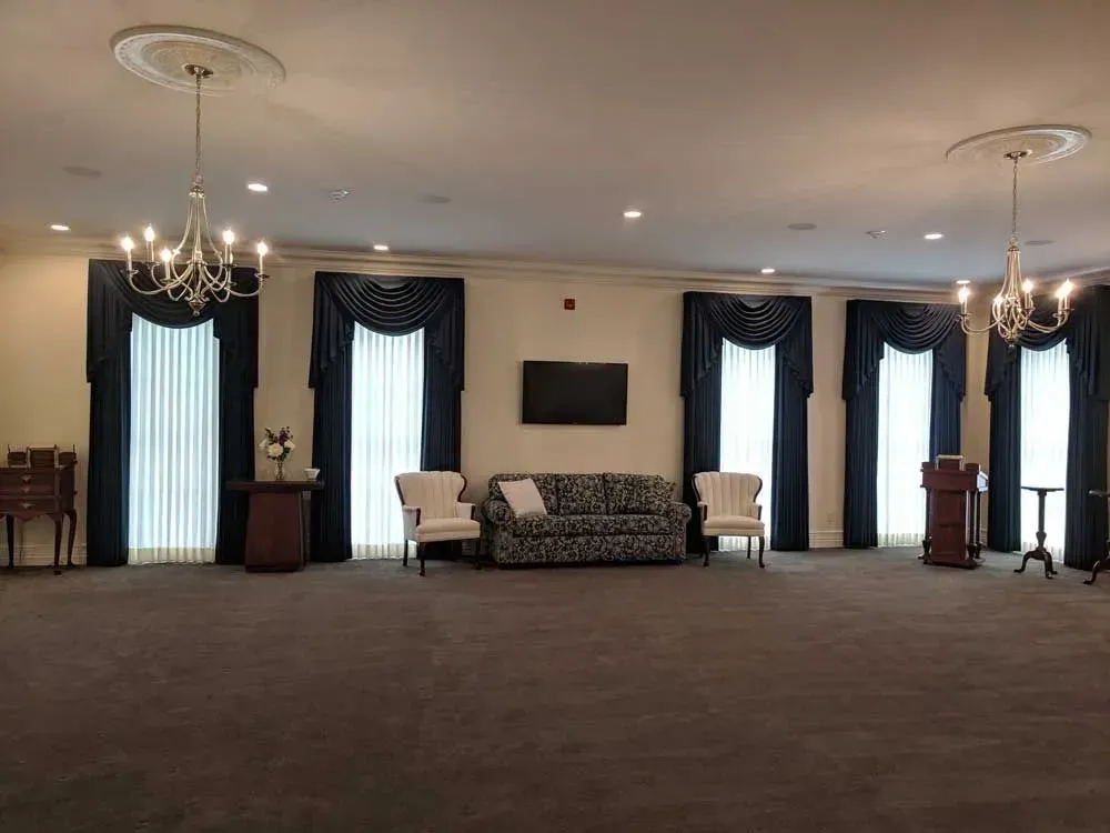 Elegant hall with chandeliers, draped windows, chairs, and a TV on the wall.