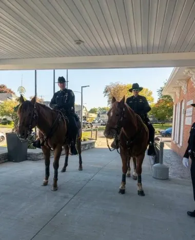 Two mounted police officers on horses under a covered walkway near a brick building