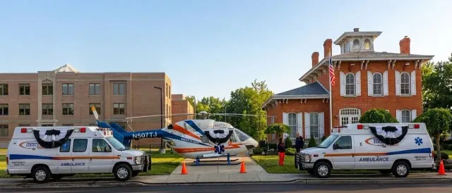 Ambulances parked outside a brick building, with cones and responders gathered around the entrance.