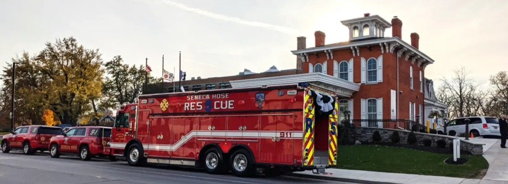 Red fire truck parked beside a brick building, with firefighters and emergency vehicles nearby.