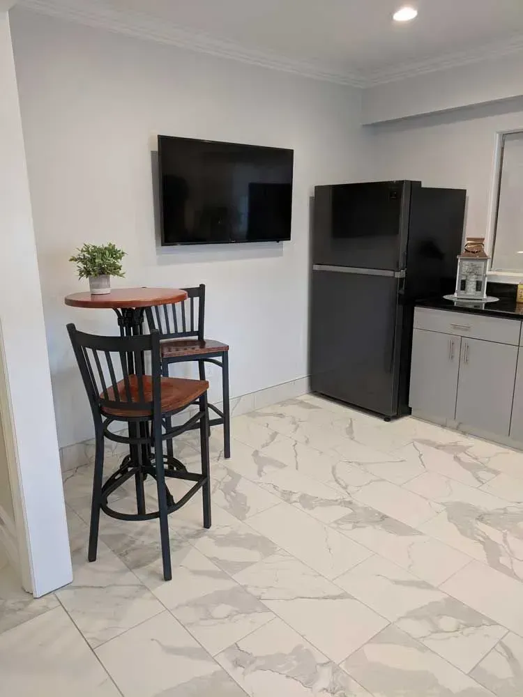 Modern kitchen nook with wall TV, black high table and stools, gray cabinets, and a black refrigerator on marble floor