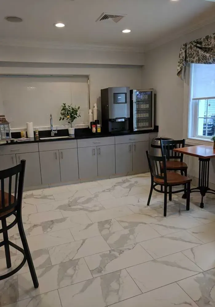 Modern kitchenette with gray cabinets, black chairs, and a marble-pattern tile floor